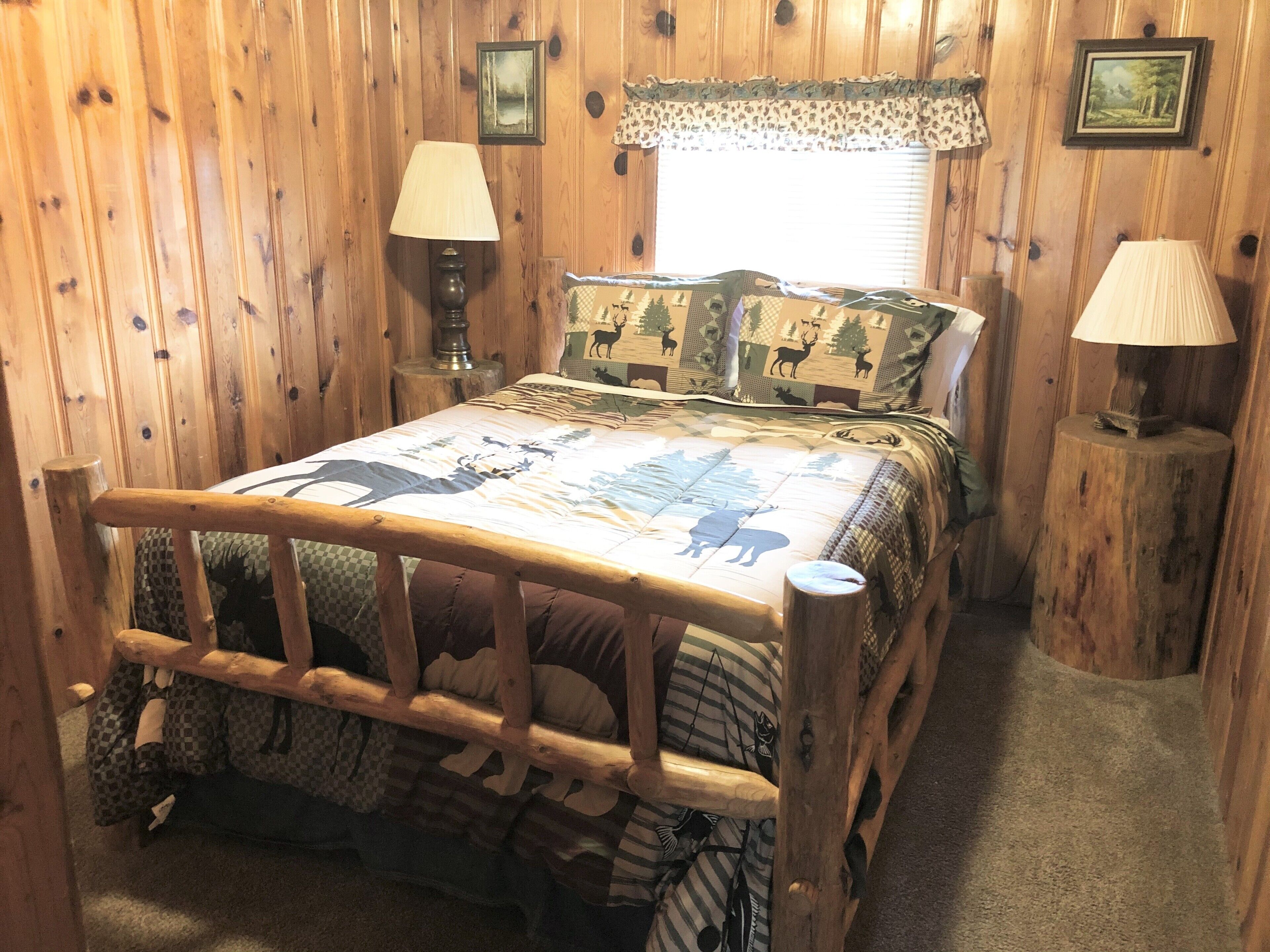 A wooden-framed bed with a checkered bedspread featuring animal prints, flanked by two bedside lamps on wooden nightstands.