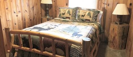 A wooden-framed bed with a checkered bedspread featuring animal prints, flanked by two bedside lamps on wooden nightstands.