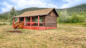 A rustic log cabin with a porch and a small staircase, surrounded by a grassy field and forested hills. - Martin's Hideout in Greer AZ (Greer)