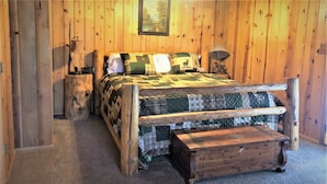 A rustic wooden room with a bed, a nightstand, a lamp, and a picture on the wall. - Martin's Hideout in Greer AZ (Greer)