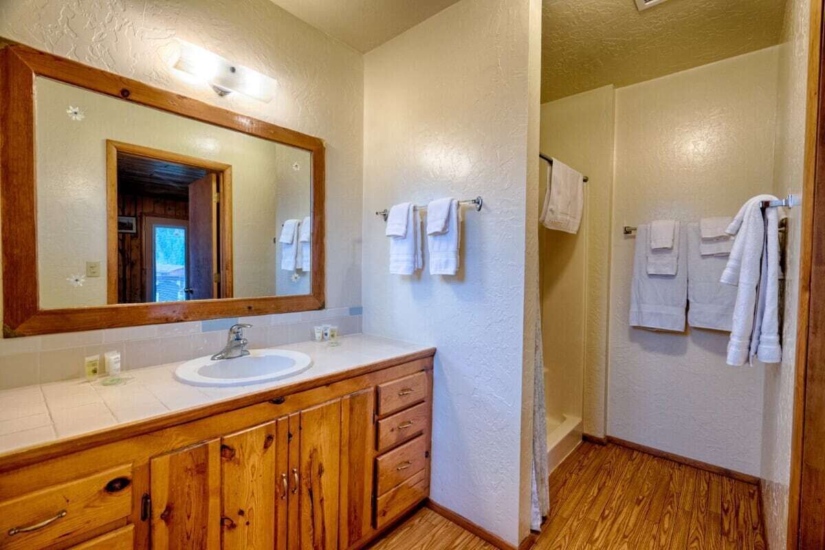 A bathroom with a wooden vanity, a large mirror, and multiple white towels hanging on the wall.