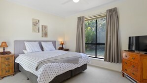 A bedroom with a bed, nightstands, a dresser, a television, and a window with curtains.