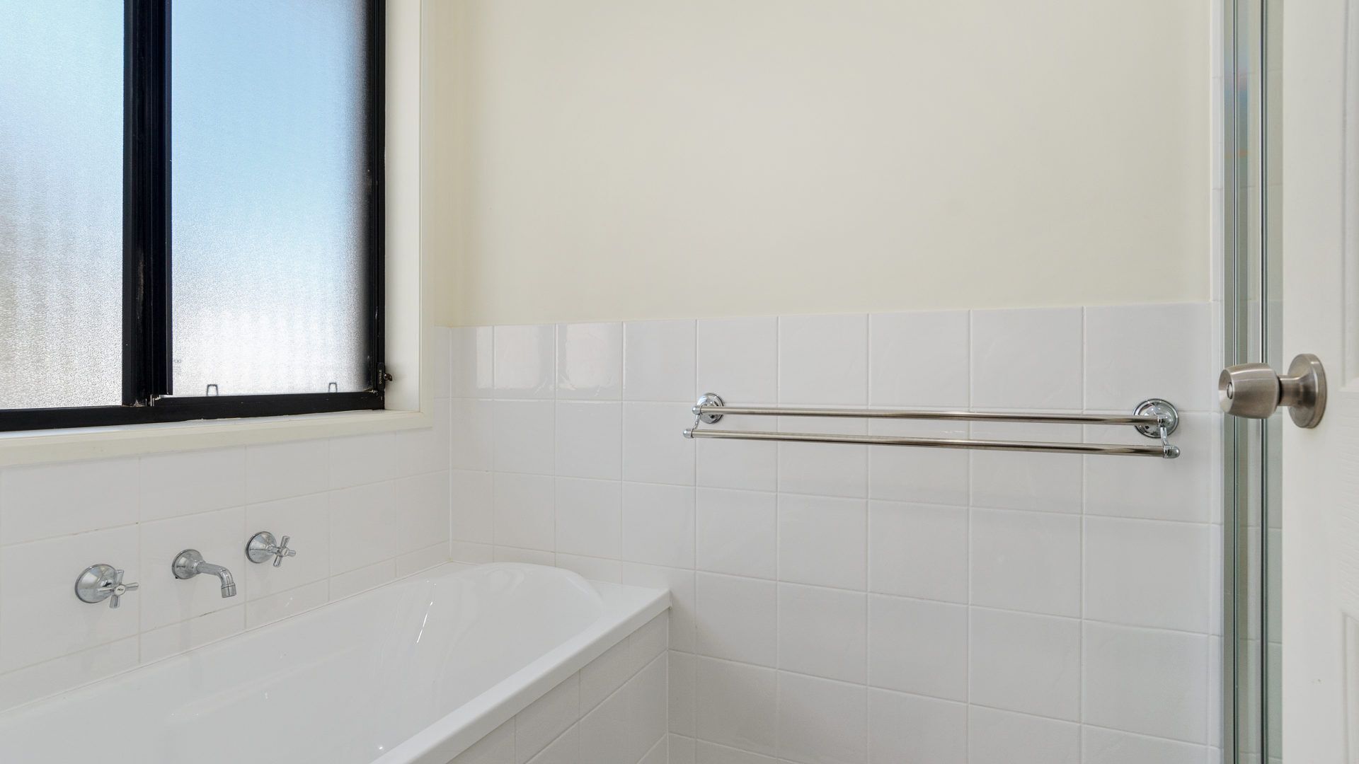 A bathroom with a white bathtub, a window with a black frame, and a towel rack.