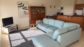 A living room with a sofa, a television, a cabinet, and a kitchen area with a microwave.