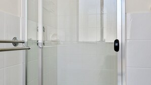 Een douche met glazen wanden, een metalen handgreep, een zichtbare douchekop en een bedieningspaneel op de deur.
