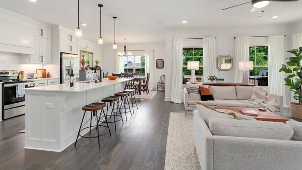 Una cocina moderna con armarios blancos, una isla central con taburetes y un comedor con mesa y sillas.