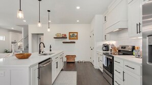 Una cocina moderna con armarios blancos, electrodomésticos de acero inoxidable, iluminación colgante y un cuenco de madera sobre la encimera.