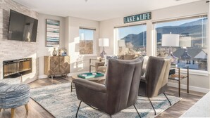 A modern living room with a fireplace, a large window with a view of mountains, and a sign that reads "LAKE LIFE". - Park Pointe C201 - Community Pool/Hot tub (Chelan)