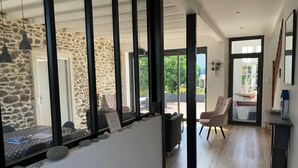 Un interior moderno con paredes de piedra, una zona de comedor con mesa y sillas, un espacio de estar con sofá, y vistas a través de amplios ventanales.