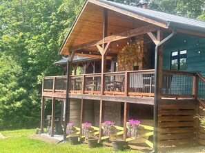 Une cabane en bois à deux étages, dotée d’un balcon, d’un mur en pierre et de jardinières suspendues.