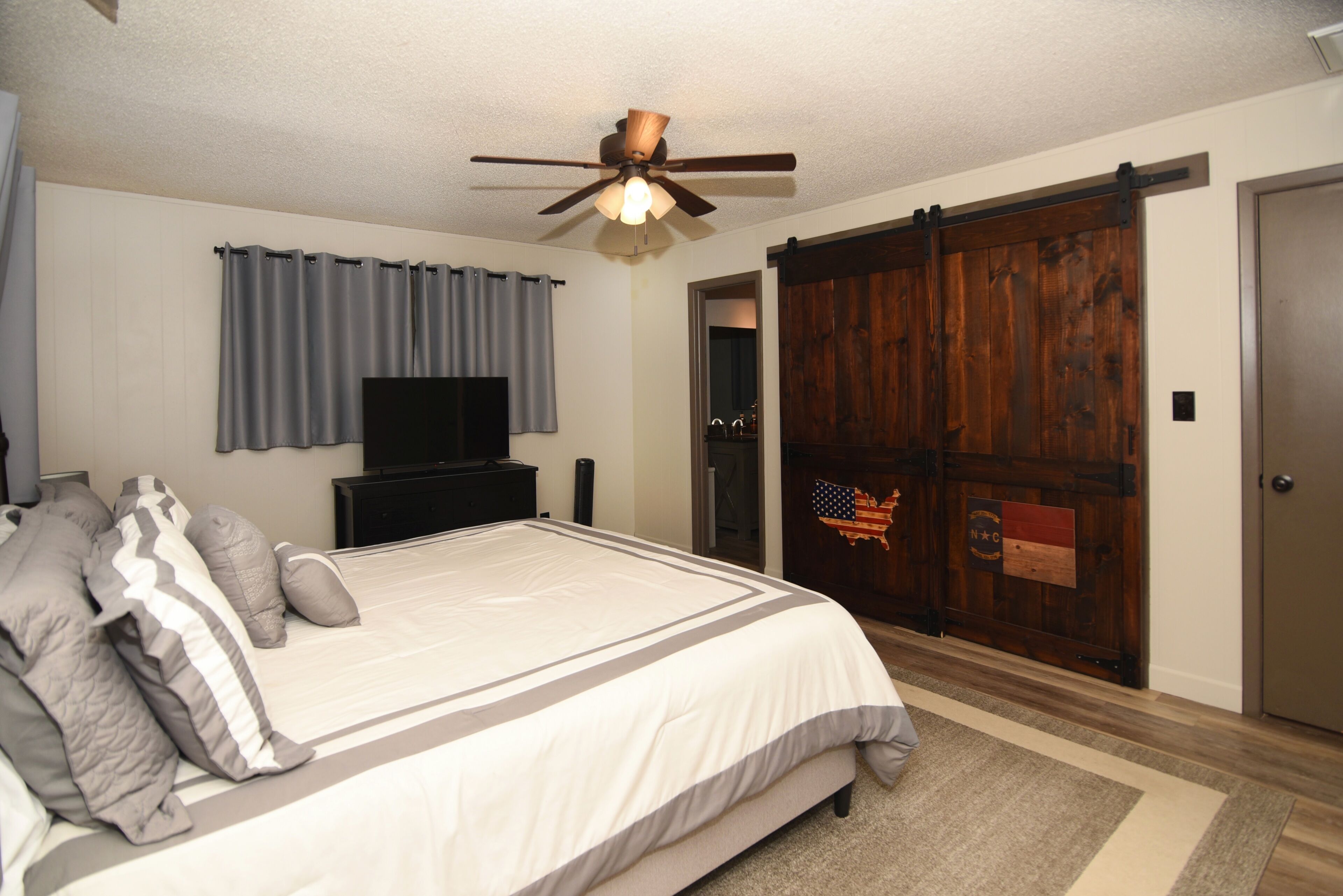 Une chambre à coucher comprenant un lit, un ventilateur de plafond, une télévision, une armoire et une porte coulissante.