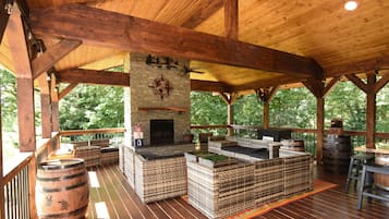A covered outdoor seating area with wooden beams, a stone fireplace, and wicker furniture.