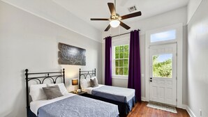 A room with two beds, a ceiling fan, a map on the wall, and a door with a view of greenery. - The Big Blue House (New Orleans)