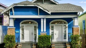 A two-story house with a blue exterior, white doors, and a front porch with steps. - The Big Blue House (New Orleans)