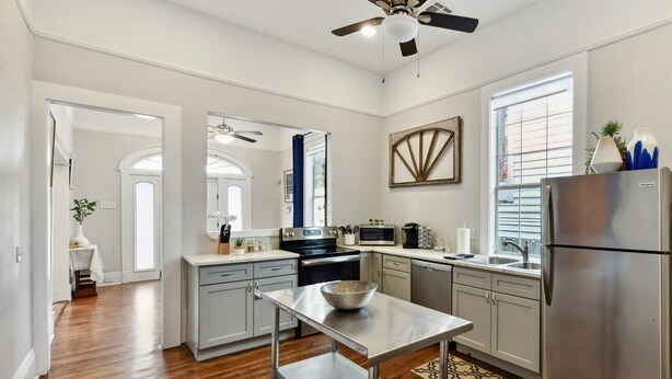 A modern kitchen with wooden flooring, stainless steel appliances, and a ceiling fan. - The Big Blue House (New Orleans)
