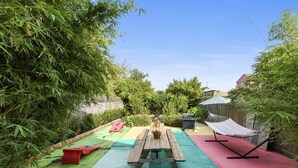A backyard with a wooden picnic table, a barbecue grill, and a hammock. - The Big Blue House (New Orleans)
