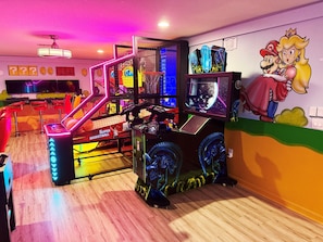 A brightly lit arcade room with neon lights, a basketball game, and a Mario and Princess Peach mural. - Disney 8BR Villa • 2 Theaters • Arcade • Pool/Spa (Kissimmee)