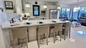Une cuisine moderne dotée d’un îlot central, de tabourets de bar et de luminaires suspendus.