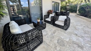 Une terrasse extérieure aménagée avec des meubles en osier, une plante en pot et une vue sur des palmiers et des immeubles.