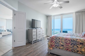 A hotel room with a bed, a TV on a dresser, a balcony with a view, and a ceiling fan.