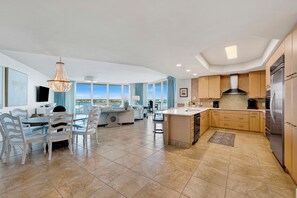 A modern kitchen with a large island, wooden cabinets, and a view of the sea.