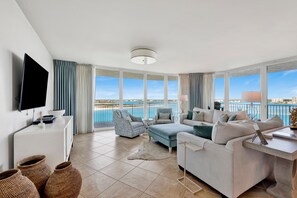 A modern living room with a flat-screen TV, a sofa set, a chair, and a view of the sea.