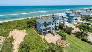 A large, light blue coastal house with a spacious front yard and a view of the ocean. - Duck Sea Sun | Oceanfront | Duck (Duck)