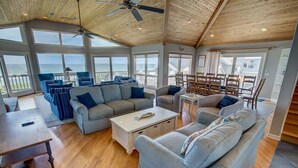A spacious living room with a high ceiling, large windows, and a view of the ocean. - Duck Sea Sun | Oceanfront | Duck (Duck)