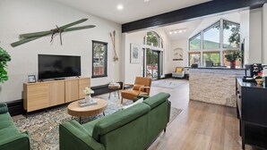A spacious living room with a large TV, green sofas, and a kitchen area with a stone wall. - Dog Friendly Vail Lionshead Studio, LH Studio (Vail)