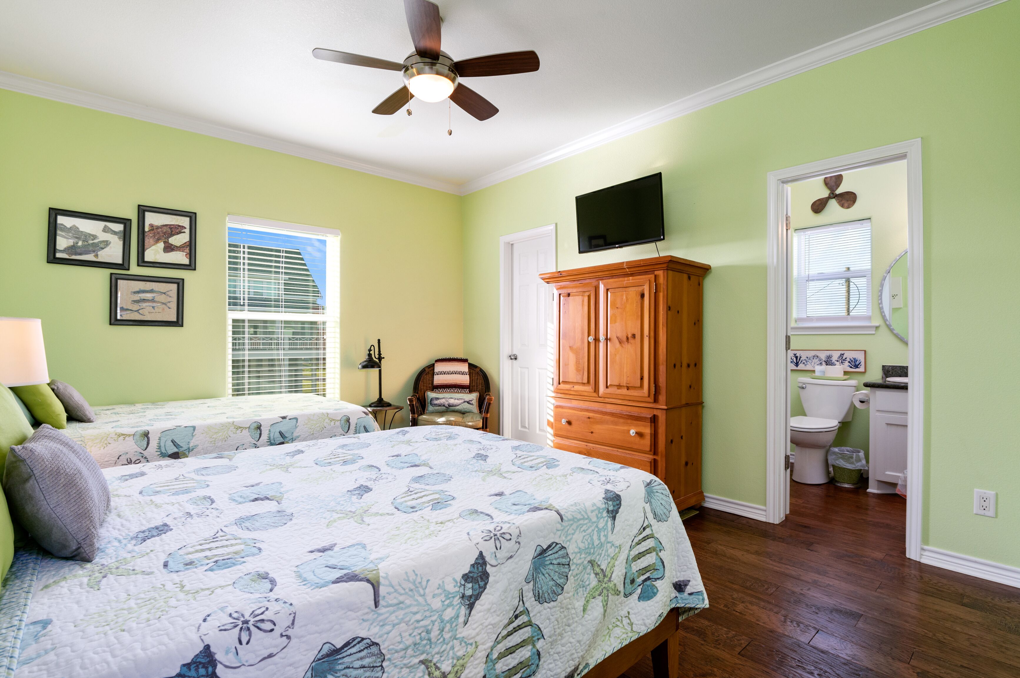 A bedroom with a bed, a ceiling fan, a wooden cabinet, a television, and a bathroom visible through an open door.