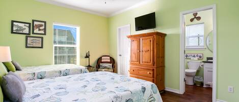 A bedroom with a bed, a ceiling fan, a wooden cabinet, a television, and a bathroom visible through an open door.