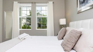 Une chambre d’hôtel avec un grand lit, des rideaux blancs, une vue sur la verdure et un tableau accroché au mur.