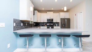 Une cuisine moderne avec des meubles blancs, un îlot central doté de tabourets, un four à micro-ondes et un réfrigérateur.