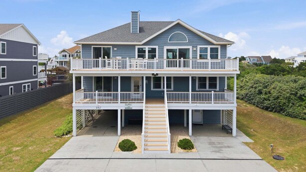 A two-story house with a balcony on the ground floor and a staircase leading to the upper level. - 1517 - Drift Inn - Steps to Beach | Pool, Hot Tub & Pet Friendly (Corolla)