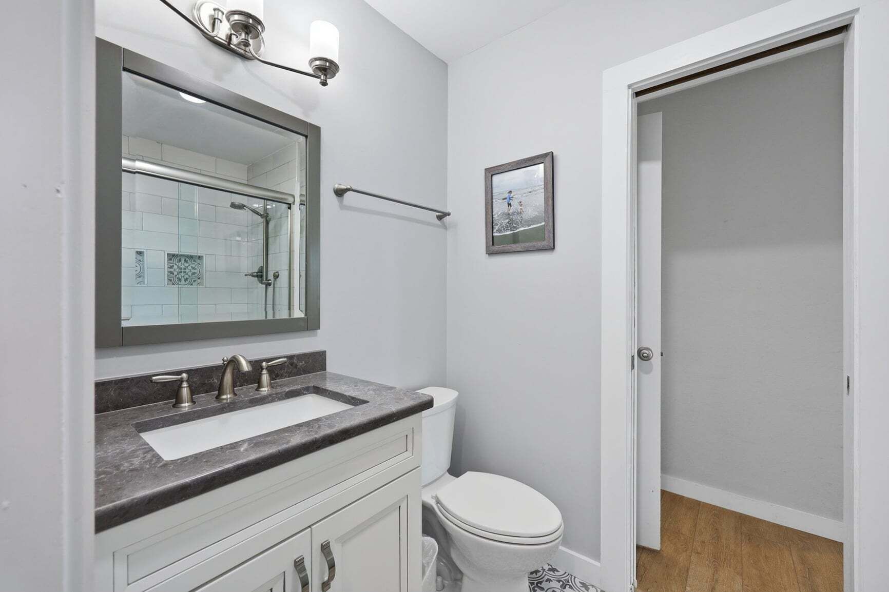 A bathroom with a white toilet, a sink with a marble countertop, a mirror, and a towel rack.