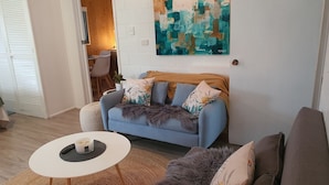 A living room with a blue sofa, a round coffee table, and a painting on the wall. - Farm Stay book  a Private Cabin - Relax Breathe Walk (Palmwoods)