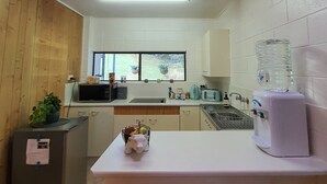 A compact kitchen with a microwave, toaster, and water dispenser. There are wooden cabinets and a window with a view of greenery. - Farm Stay book  a Private Cabin - Relax Breathe Walk (Palmwoods)