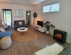 Relax in this stylish living room with a comfortable sofa, armchair, and fireplace, surrounded by lush greenery and natural light.