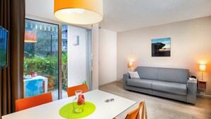 Een moderne woonkamer met een grijze bank, een eettafel met oranje stoelen en een groot raam met uitzicht op groen.