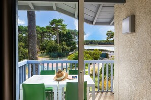 A balcony with a white table and green chairs, overlooking a lush landscape with trees and a body of water.