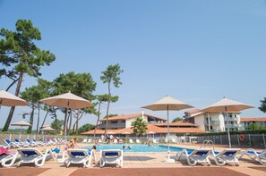 A poolside area with lounge chairs and umbrellas, surrounded by buildings and trees.