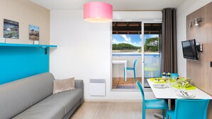 Une pièce moderne avec un canapé gris, des chaises turquoise, une table à manger blanche mise en place avec des assiettes et des verres, une suspension rose et un téléviseur fixé au mur.