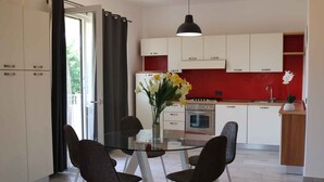 Una cucina moderna con mobili bianchi, uno schienale rosso e un tavolo da pranzo in vetro con quattro sedie.