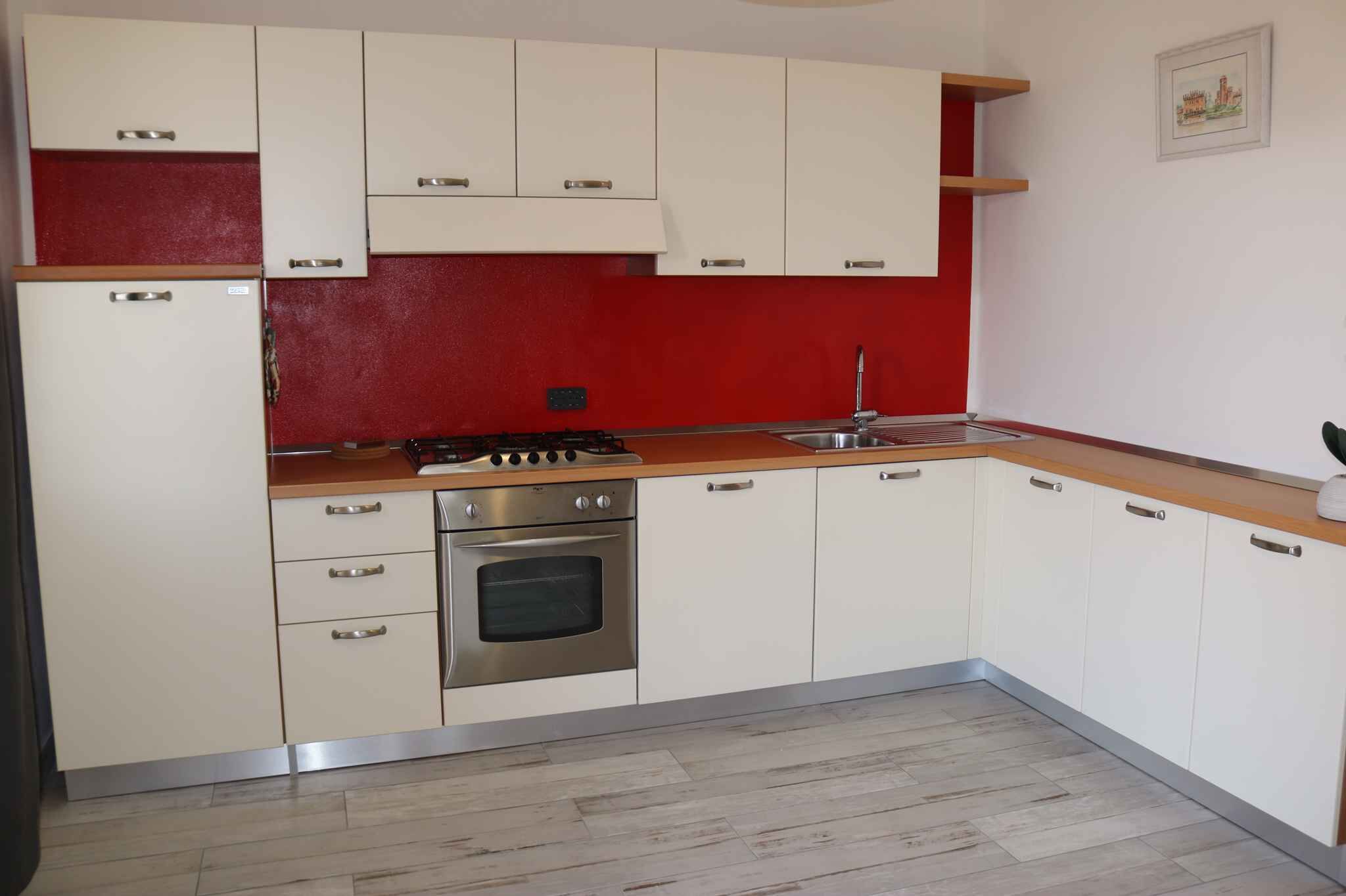 A kitchen with white cabinets, a red backsplash, a stainless steel stove, and a sink.