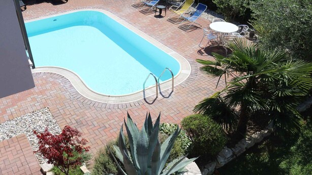 Una piscina con lettini e un tavolo, circondata da piante e un muro in pietra.