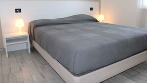 Una camera da letto moderna con un letto grande, due comodini con lampade e un pavimento in legno chiaro.