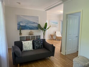 A living room with a dark grey sofa, two cushions with abstract designs, a white console table with decorative items, and a large abstract painting on the wall. - Pearl Bliss, a sundrenched, secluded oasis 200m from spectacular Pearl Beach (Pearl Beach)