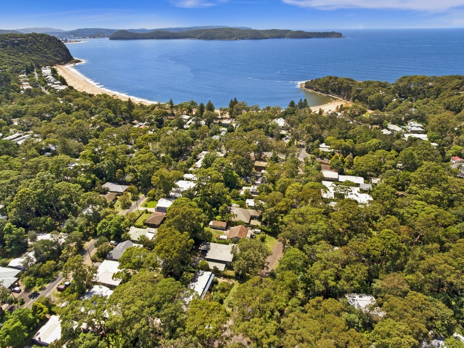 An aerial view of a residential area with houses surrounded by dense greenery, a beach, and a clear blue sea.