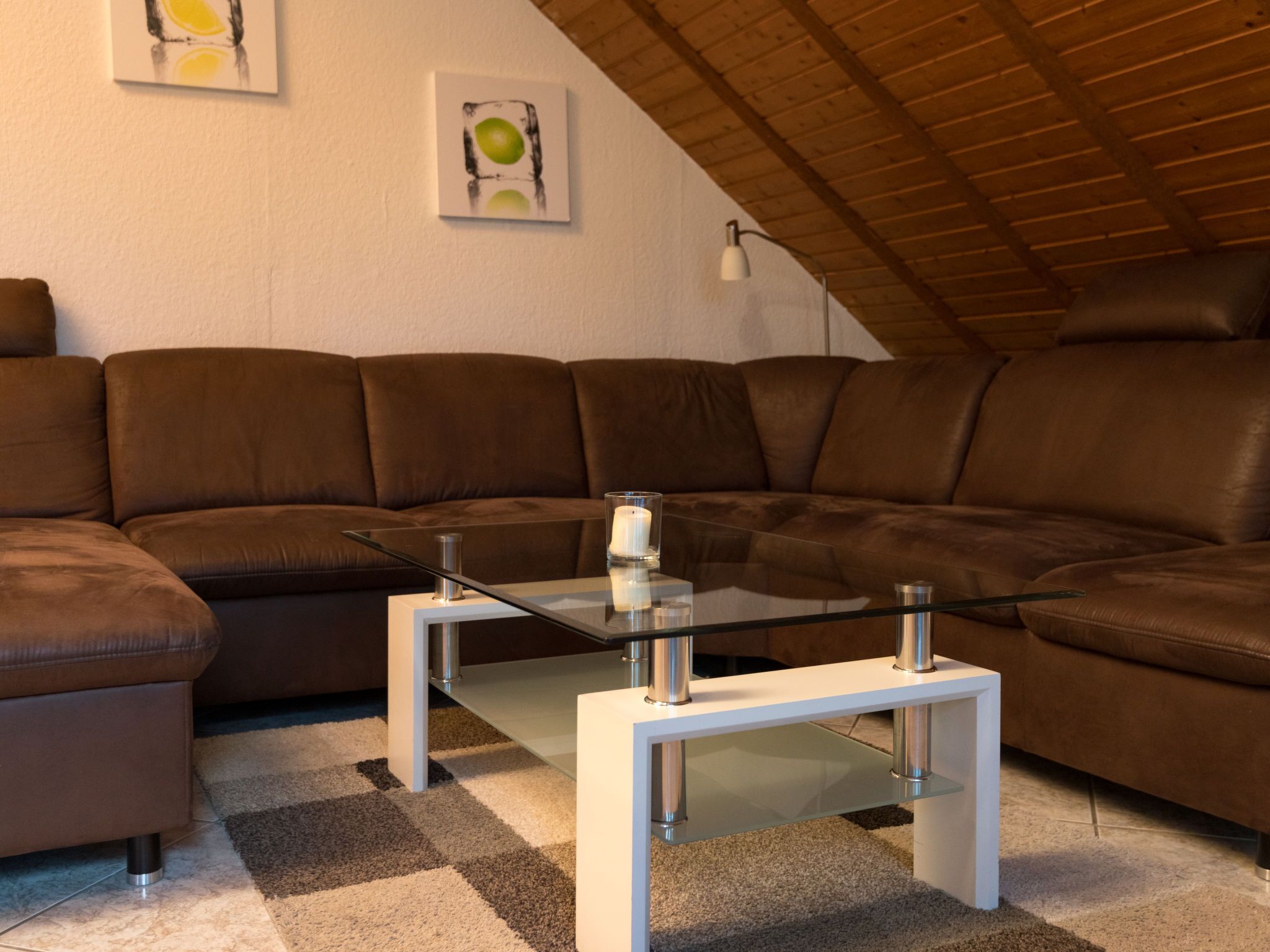Een moderne woonkamer met een bruine leren modulaire bank, een glazen salontafel en een kamerkleed met een patroon.