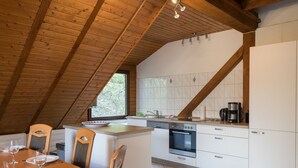 Une cuisine avec des meubles blancs, un plafond en bois et un coin repas avec une table dressée pour deux personnes.